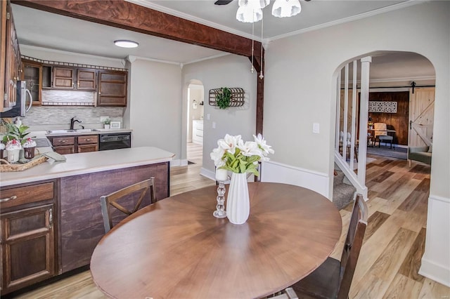 dining room with a barn door, arched walkways, light wood-style flooring, and crown molding