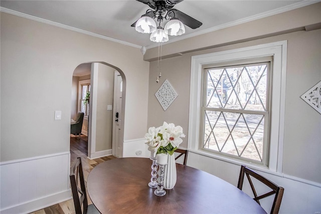 dining room with arched walkways, crown molding, ceiling fan, and wood finished floors