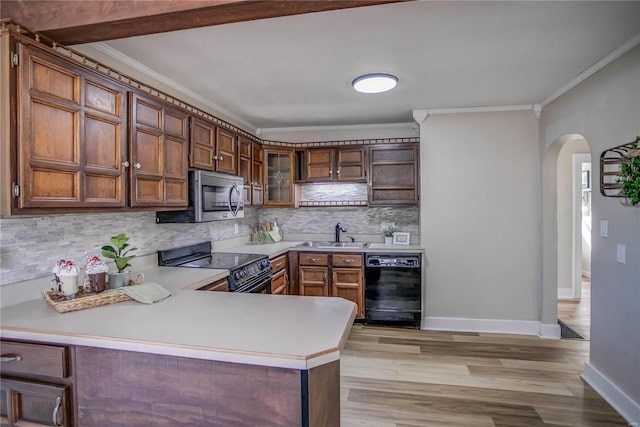 kitchen featuring light wood-style flooring, arched walkways, a sink, black appliances, and light countertops