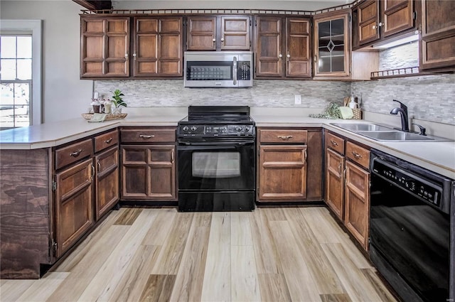 kitchen featuring light countertops, light wood-style flooring, a peninsula, black appliances, and a sink