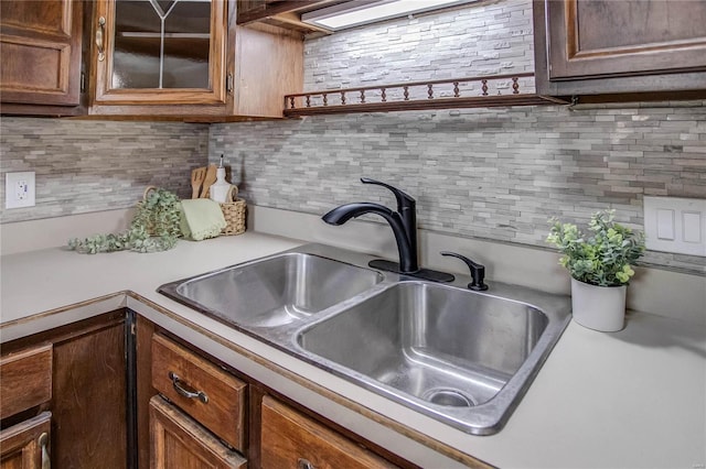 kitchen featuring light countertops, glass insert cabinets, tasteful backsplash, and a sink