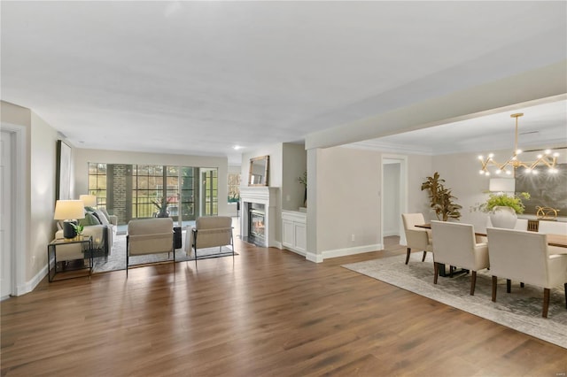 living room with a glass covered fireplace, baseboards, an inviting chandelier, and wood finished floors