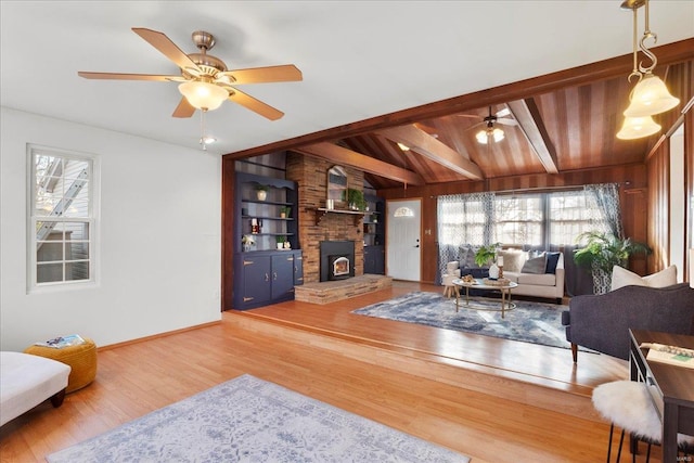 living room featuring wood finished floors, baseboards, vaulted ceiling with beams, a fireplace, and ceiling fan