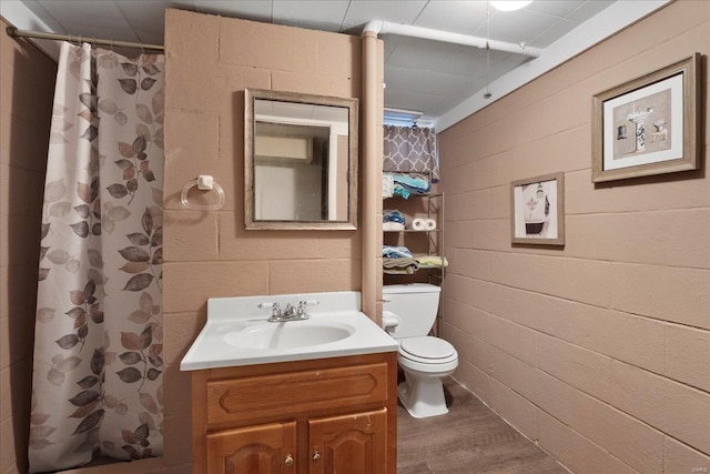 full bathroom with toilet, a shower with shower curtain, wood finished floors, vanity, and concrete block wall