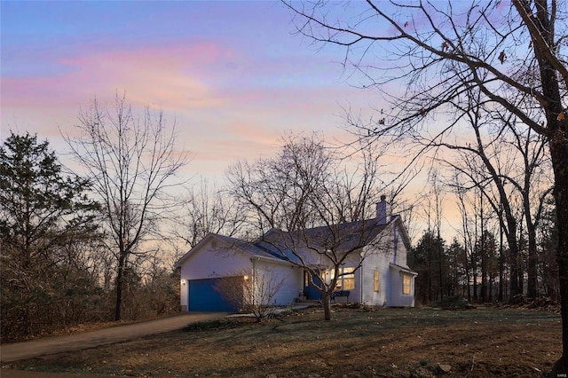 property exterior at dusk featuring a yard, dirt driveway, a chimney, and an attached garage