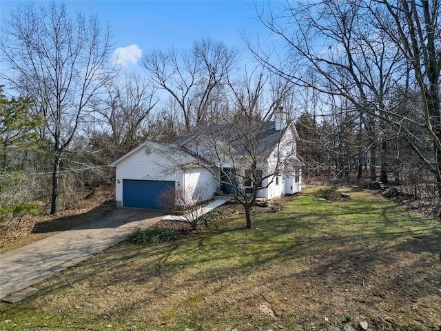 view of side of property with a yard, driveway, a chimney, and an attached garage