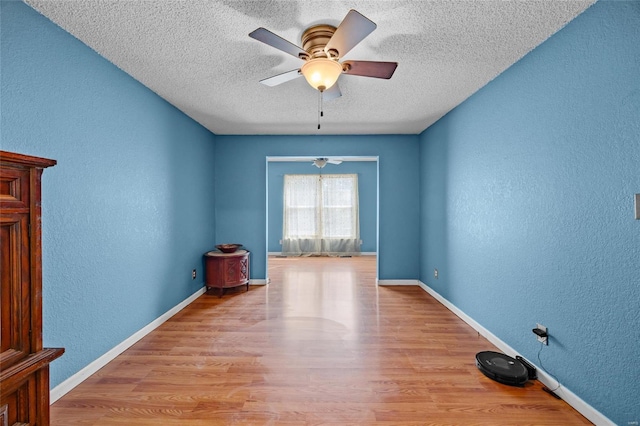 spare room featuring a textured ceiling, light wood finished floors, baseboards, ceiling fan, and a textured wall