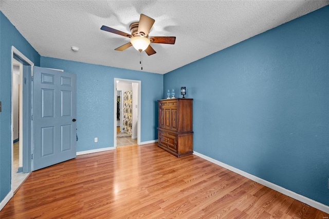 unfurnished bedroom featuring baseboards, light wood-style floors, a textured wall, a textured ceiling, and a ceiling fan