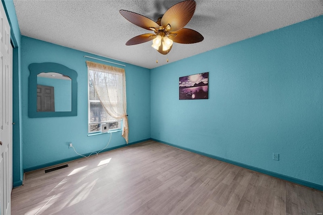 unfurnished room with visible vents, baseboards, wood finished floors, a textured ceiling, and a ceiling fan