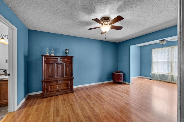 spare room with a textured ceiling, wood finished floors, ceiling fan, and baseboards