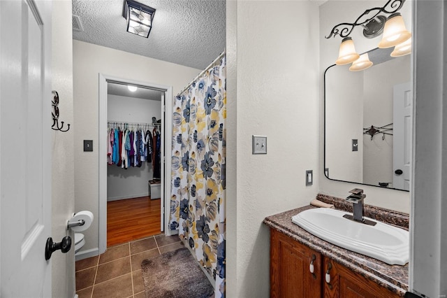 bathroom with a textured ceiling, vanity, curtained shower, a walk in closet, and tile patterned floors