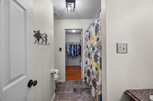 bathroom featuring a textured ceiling, a shower with curtain, toilet, tile patterned floors, and a textured wall