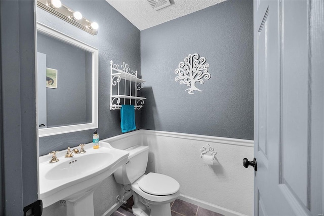 half bathroom featuring a textured wall, a textured ceiling, toilet, visible vents, and a sink