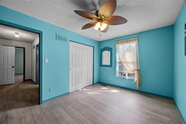 unfurnished bedroom with visible vents, baseboards, a closet, a textured ceiling, and wood finished floors