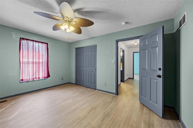 unfurnished bedroom featuring light wood-type flooring, a closet, a textured ceiling, visible vents, and baseboards