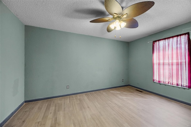 spare room featuring a textured ceiling, a ceiling fan, visible vents, wood finished floors, and baseboards