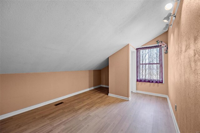 bonus room featuring visible vents, baseboards, a textured ceiling, vaulted ceiling, and wood finished floors