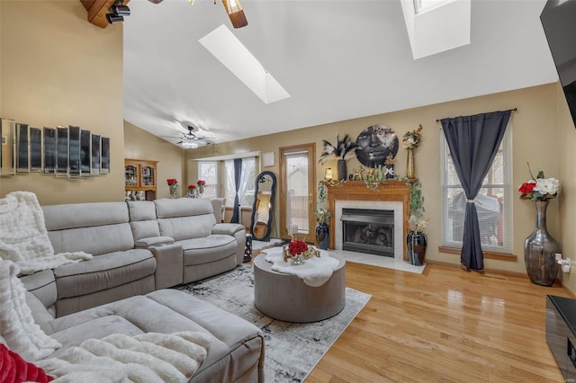 living room featuring a fireplace with flush hearth, high vaulted ceiling, wood finished floors, a skylight, and ceiling fan