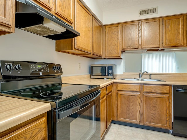 kitchen featuring visible vents, under cabinet range hood, light countertops, black appliances, and a sink