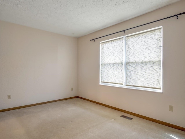 spare room with light colored carpet, baseboards, and a textured ceiling