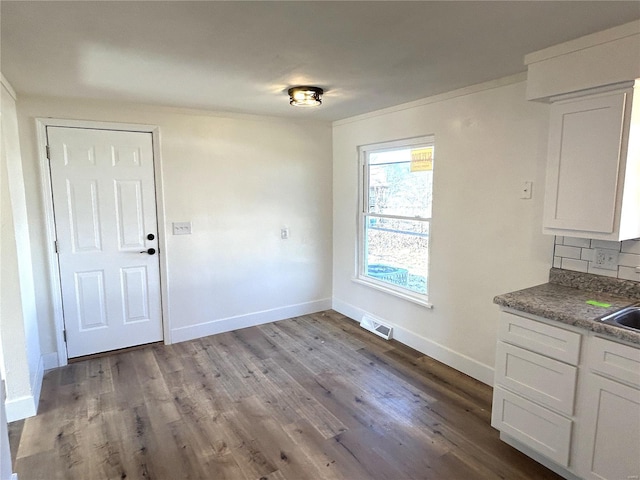 unfurnished dining area with wood finished floors, visible vents, baseboards, a sink, and crown molding