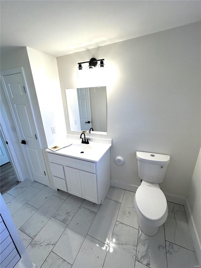 bathroom with vanity, toilet, baseboards, and marble finish floor