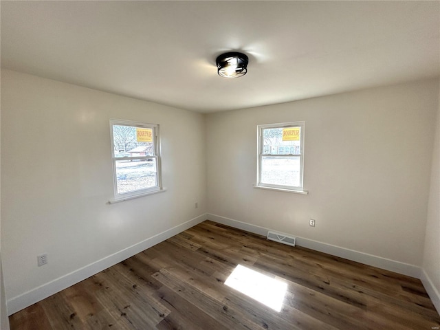 unfurnished room featuring visible vents, plenty of natural light, baseboards, and wood finished floors