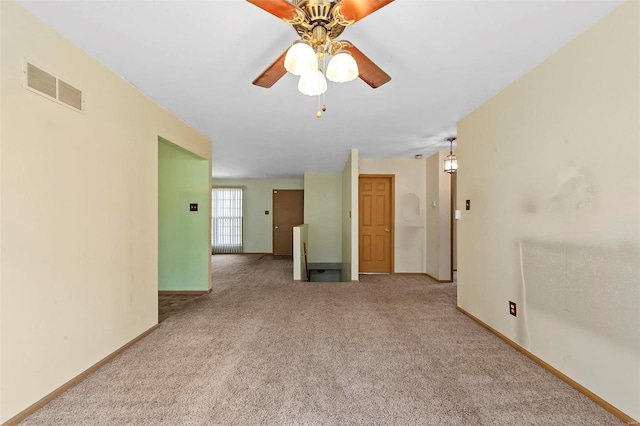 carpeted spare room with visible vents, baseboards, and ceiling fan