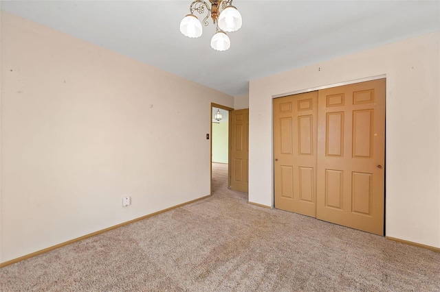 unfurnished bedroom with a notable chandelier, carpet flooring, baseboards, and a closet
