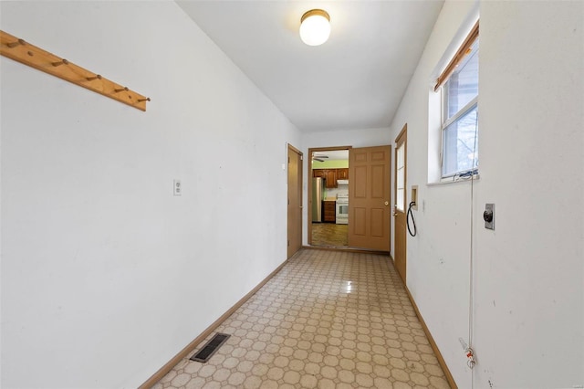 hallway featuring visible vents, baseboards, and light floors