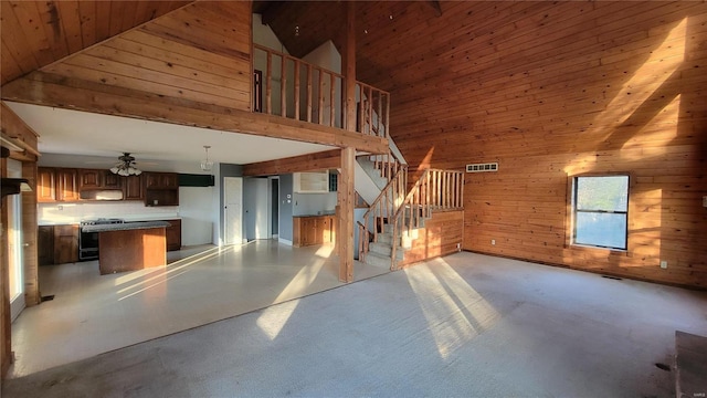 unfurnished living room with stairs, high vaulted ceiling, a ceiling fan, wooden walls, and visible vents