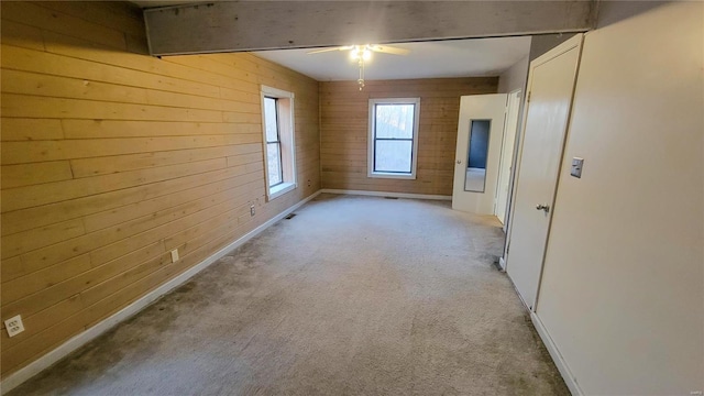 spare room featuring light colored carpet, wood walls, baseboards, and a ceiling fan