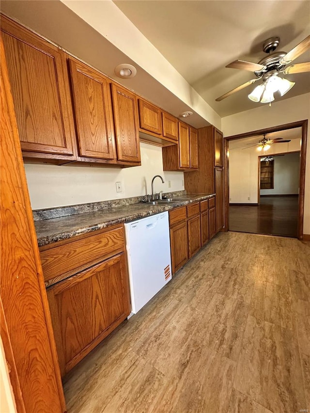 kitchen featuring light wood finished floors, dark countertops, white dishwasher, brown cabinetry, and a sink