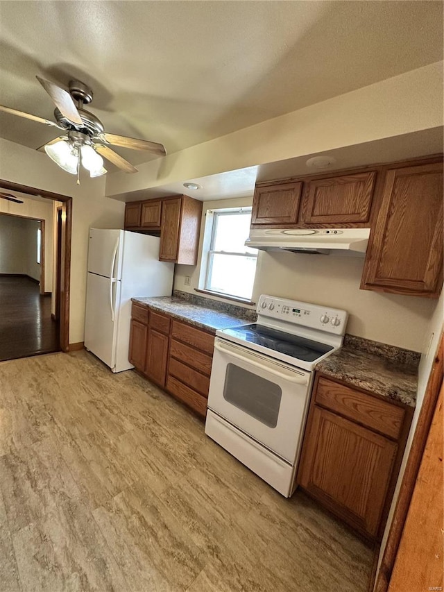 kitchen with a ceiling fan, under cabinet range hood, dark countertops, white appliances, and brown cabinetry