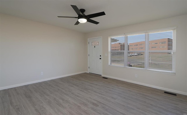 spare room featuring wood finished floors, baseboards, visible vents, and ceiling fan