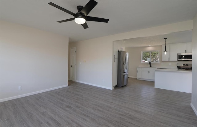 unfurnished living room with wood finished floors, baseboards, a ceiling fan, and a sink