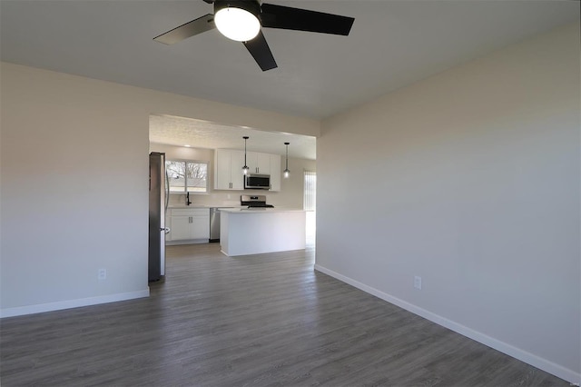 unfurnished living room with baseboards, dark wood-type flooring, a ceiling fan, and a sink