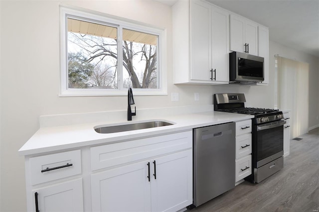 kitchen featuring light countertops, stainless steel appliances, light wood-style floors, white cabinetry, and a sink