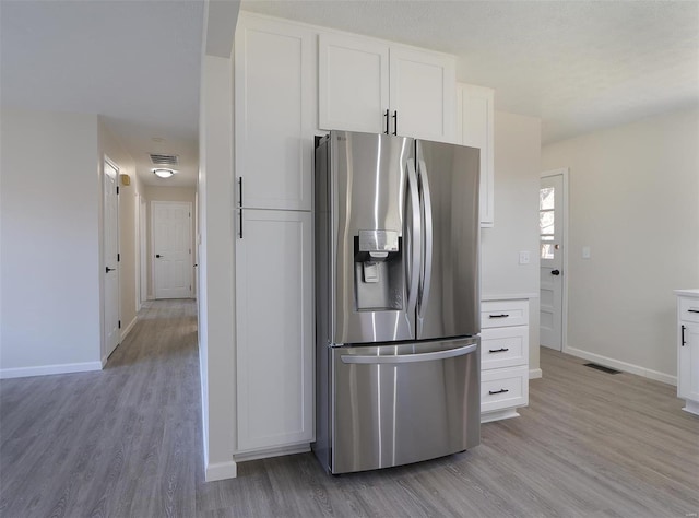 kitchen with visible vents, baseboards, light wood-type flooring, white cabinets, and stainless steel fridge