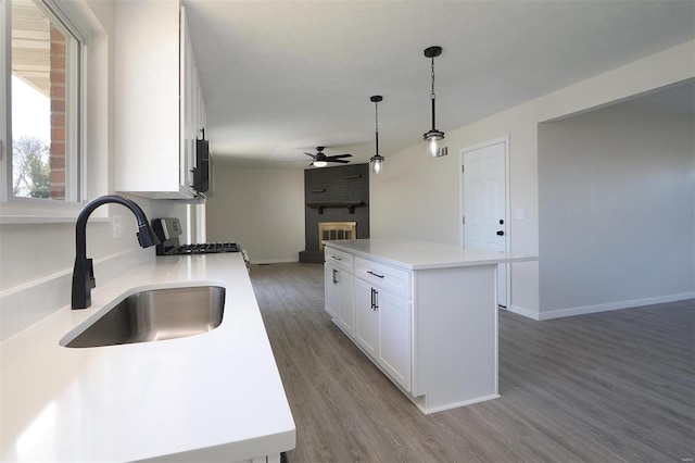 kitchen featuring a ceiling fan, a sink, wood finished floors, open floor plan, and a fireplace