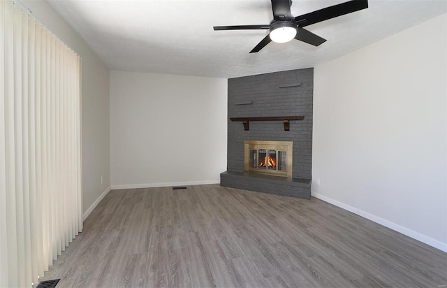 unfurnished living room with visible vents, wood finished floors, a fireplace, baseboards, and ceiling fan