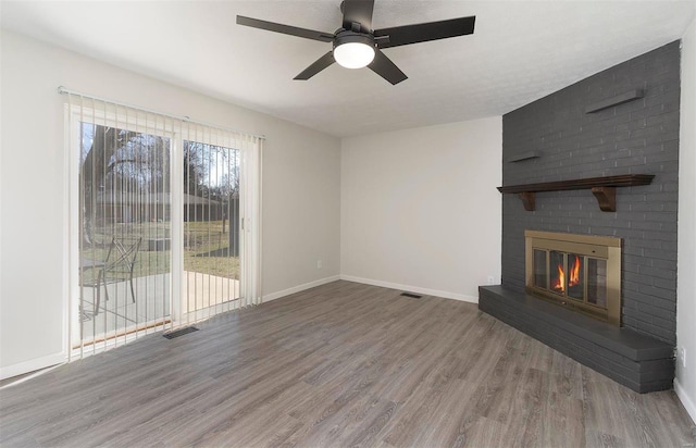 unfurnished living room featuring a ceiling fan, visible vents, wood finished floors, baseboards, and a brick fireplace