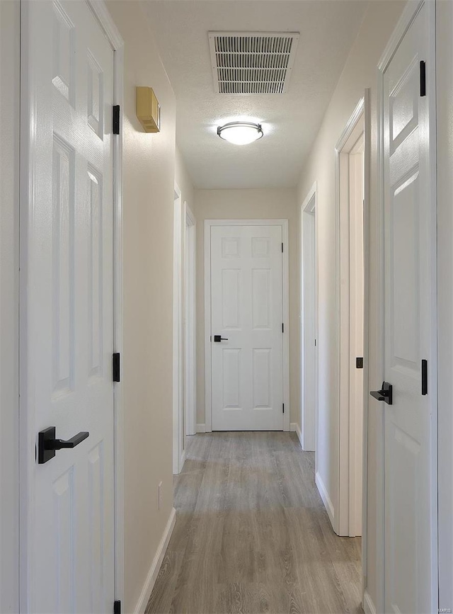 corridor with visible vents, light wood-style flooring, and baseboards