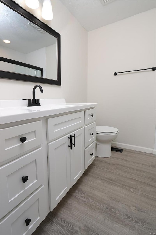 bathroom featuring toilet, vanity, baseboards, and wood finished floors