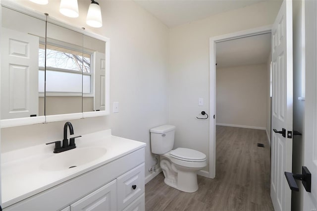 bathroom with vanity, toilet, wood finished floors, and baseboards