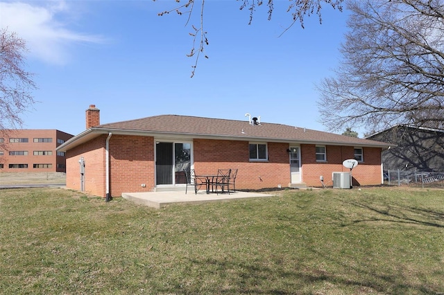 back of property featuring a chimney, a patio area, brick siding, and a lawn