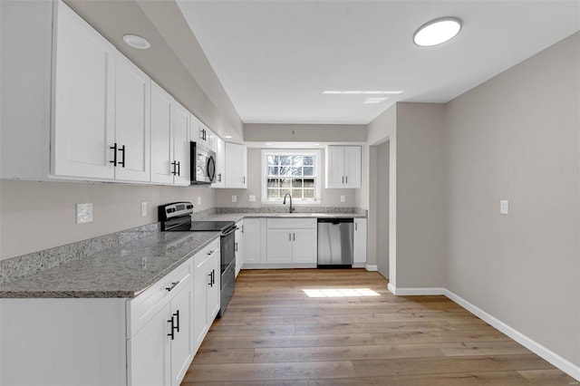 kitchen with baseboards, light stone countertops, light wood-type flooring, white cabinets, and stainless steel appliances