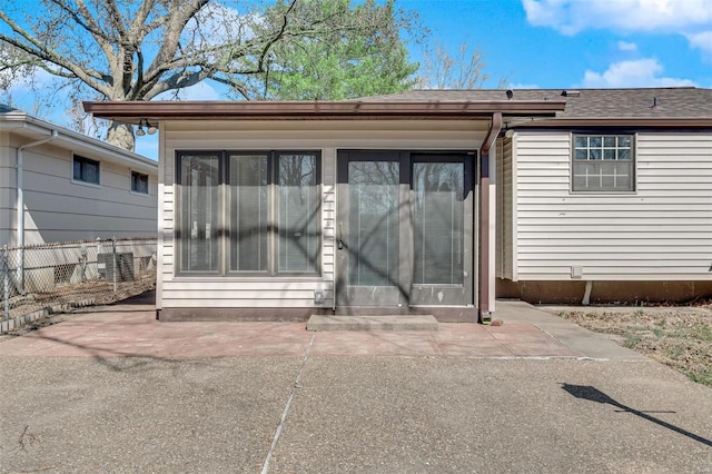 entrance to property with a patio, fence, and a shingled roof