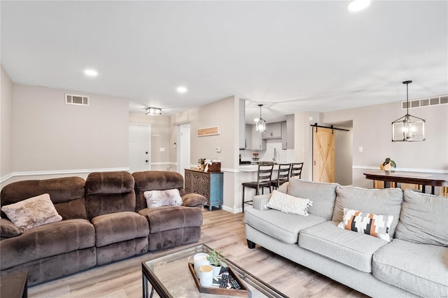 living area with recessed lighting, a barn door, visible vents, and light wood finished floors