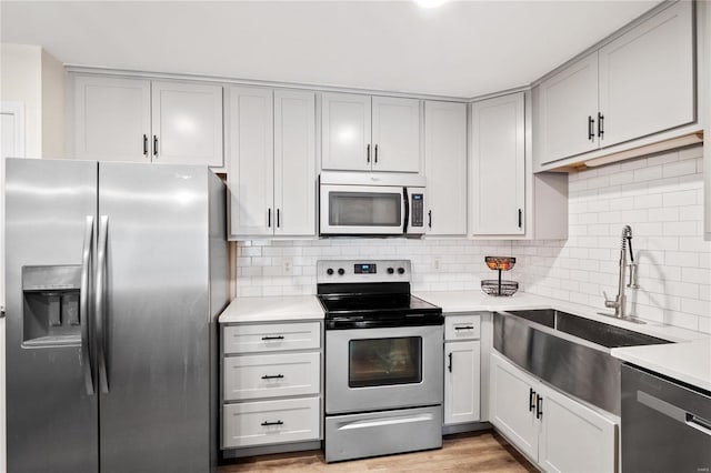 kitchen with a sink, decorative backsplash, light countertops, light wood-style floors, and appliances with stainless steel finishes